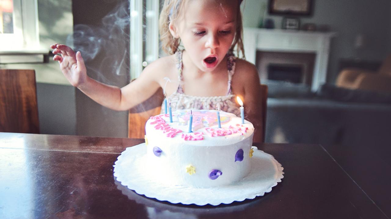 Dziewczynka, któa ma urodziny zdmuchuje świeczki na torcie