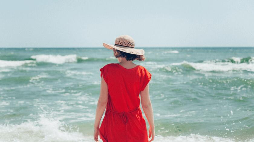 mloda kobieta na plazy w kapeluszu w czerwonej sukience morze fale lato moda