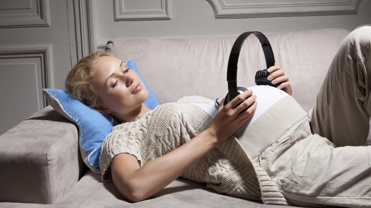 Kobieta w ciąży przystawia do brzucha słuchawki