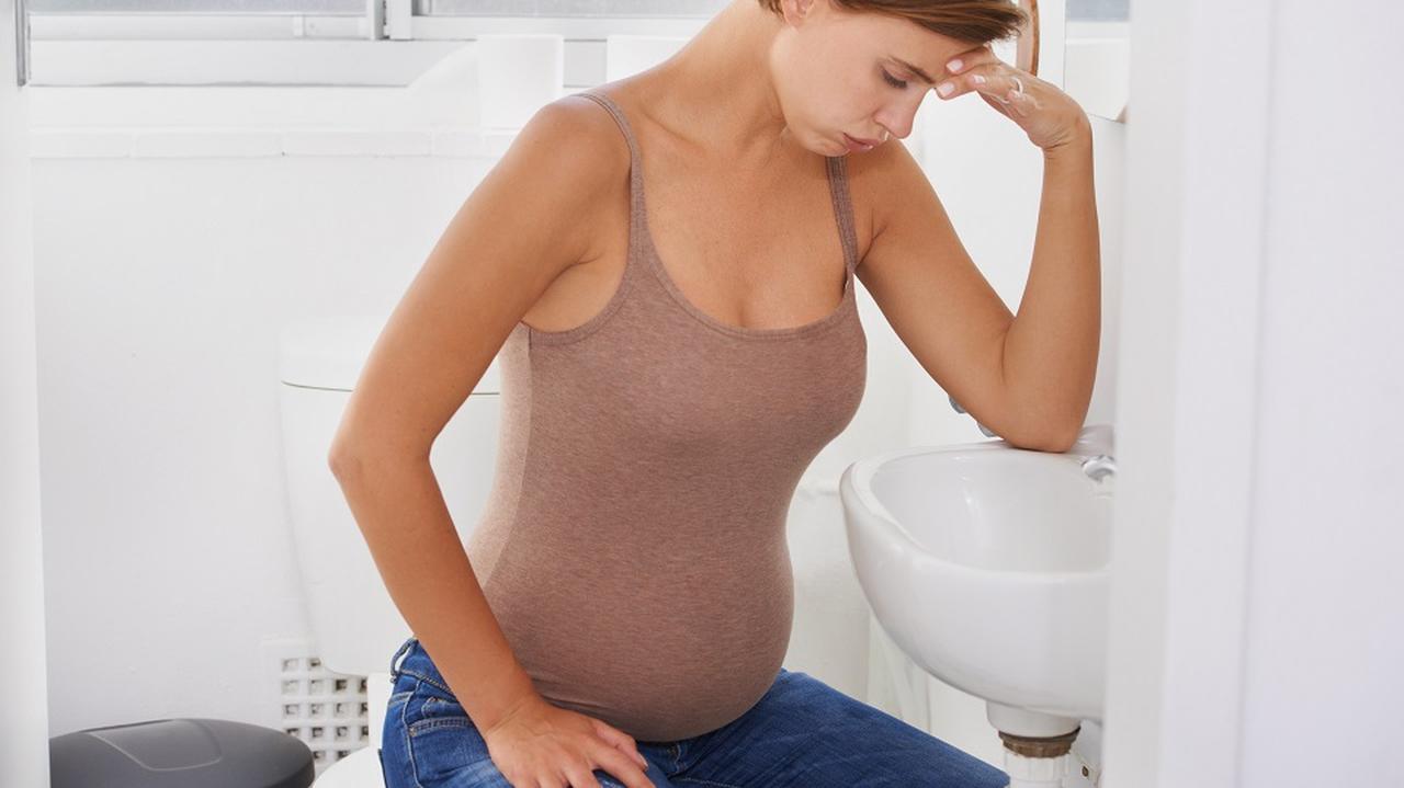 Kobieta w ciąży siedzi nad zlewem. Ma odruch wymiotny.