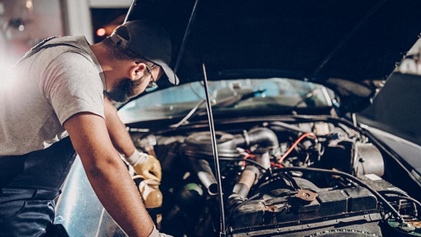 Mężczyzna w rękawicach oparty o auto przygląda się silnikowi