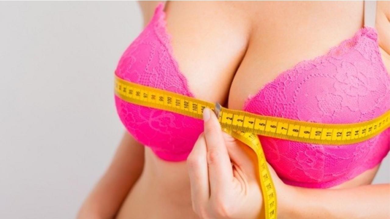 Kobieta z dużymi piersiami w różowym staniku mierzy obwód biustu za pomocą miarki krawieckiej
