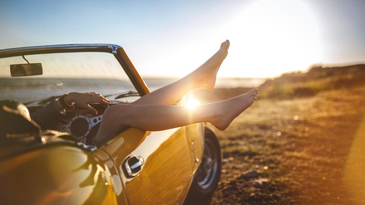kobiece stopy wystają z żółtego samochodu cabrio na tle zachodzącego słońca