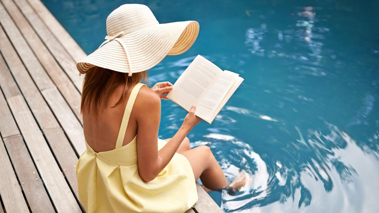 Dziewczyna w letniej sukience czyta książkę nad brzegiem basenu