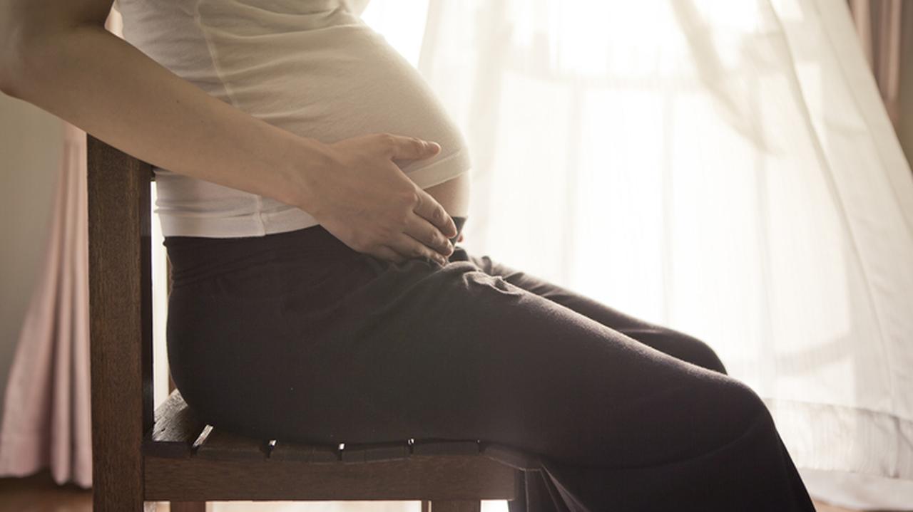 Kobieta w ciąży siedzi na krześle i trzyma się za brzuch