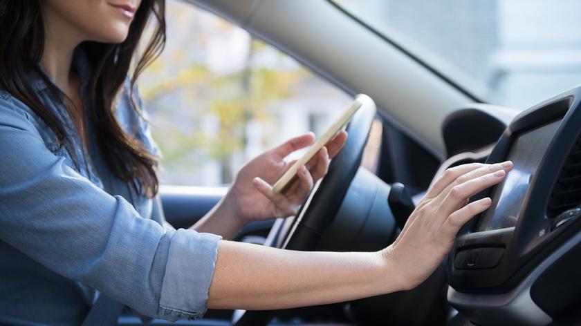 kobieta prowadzi samochód i trzyma w ręce telefon