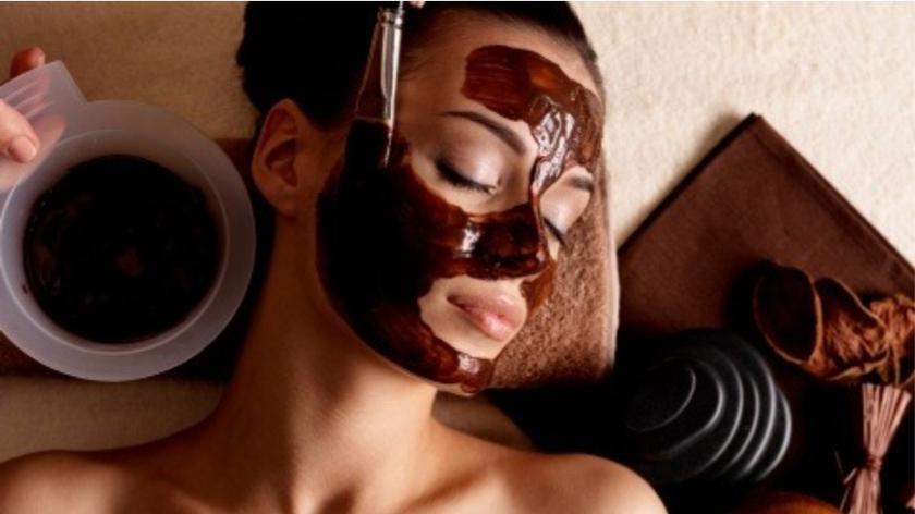 Kobieta z maską z czekolady na twarzy, otoczona czekoladowymi przysmakami