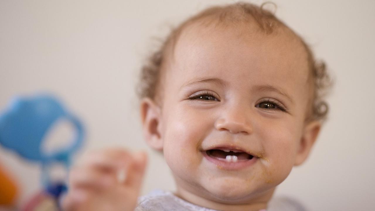 Ząbkujące dziecko pokazuje w uśmiechu swoje pierwsze ząbki