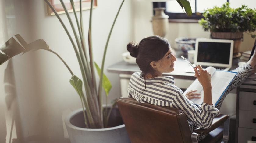 Kobieta siedzi na krześle przy biurku z ołówkiem w ręku i myśli