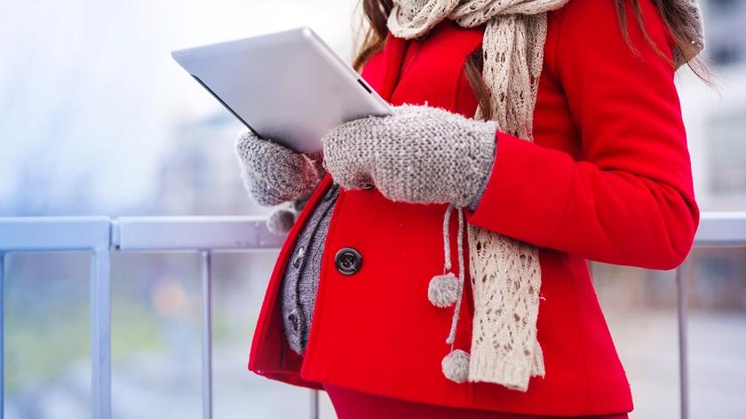 Kobieta w ciąży w czerwonym płaszczu i szarym swetrze. 