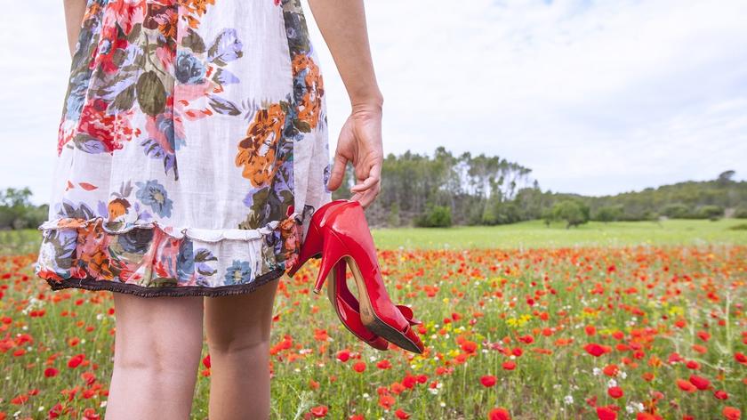 Spódnica w kwiaty - kobieta w spódnicy trzyma czerwone szpilki w dłoni. W tle łąka.