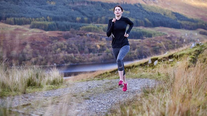 Kobieta biegnie przez łąkę. Ścieżka dla biegaczy.