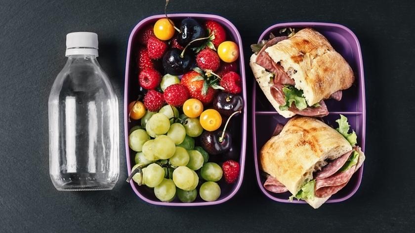 Lunch box do pracy, w nim dwie kanapki, owoce i butelka wody