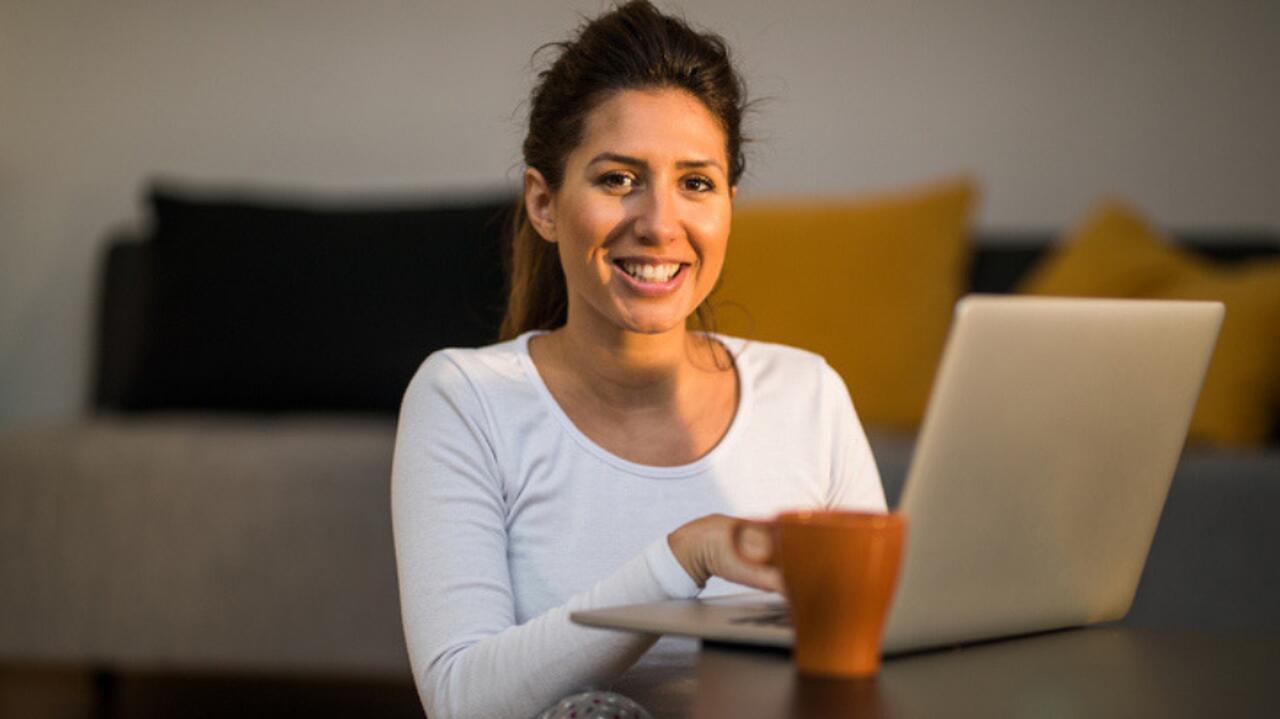 usmiechnieta kobieta siedzi przy niskim stoliku z laptopem i kubkiem