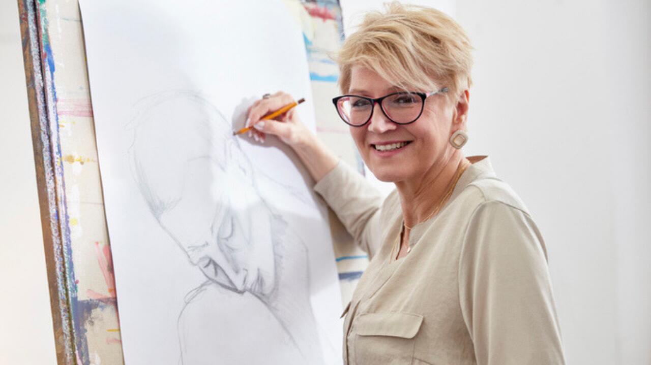 kobieta w srednim wieku przed sztalugami rysuje portret kobiety usmiechnieta