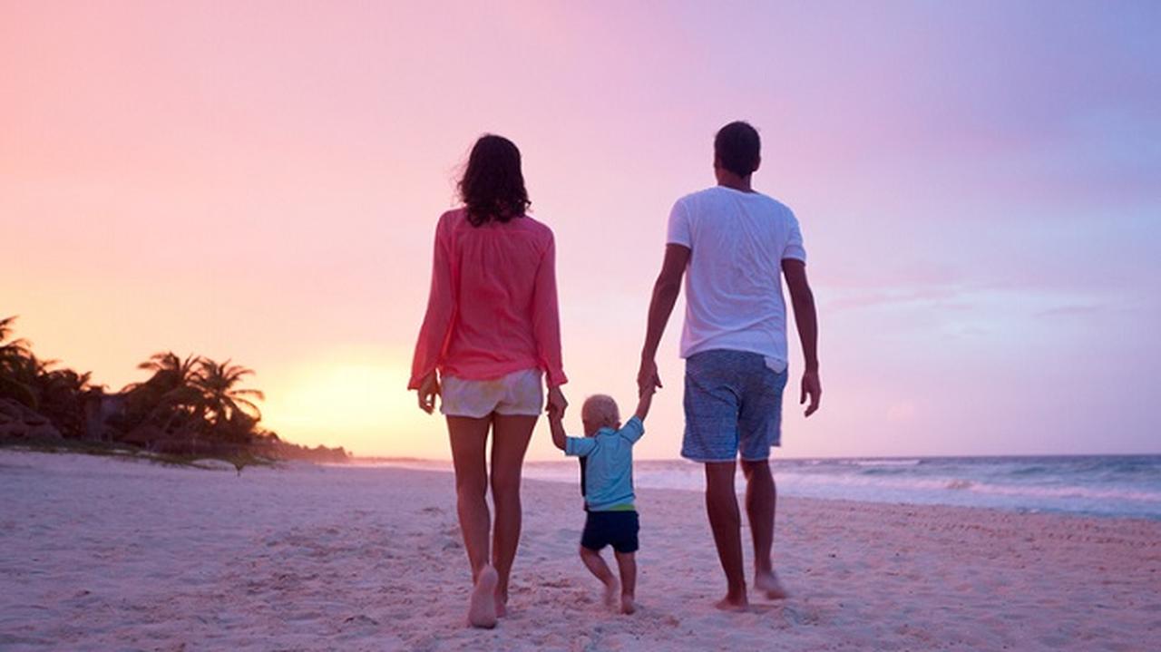 Rodzice ida z niemowlakiem po plaży, zachodzące słońce w tle