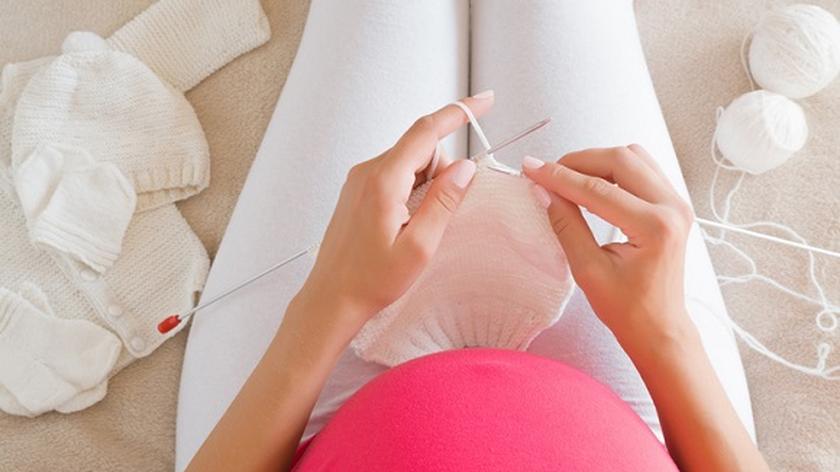 Ciężarna kobieta robi na drutach ubranko dla dziecka