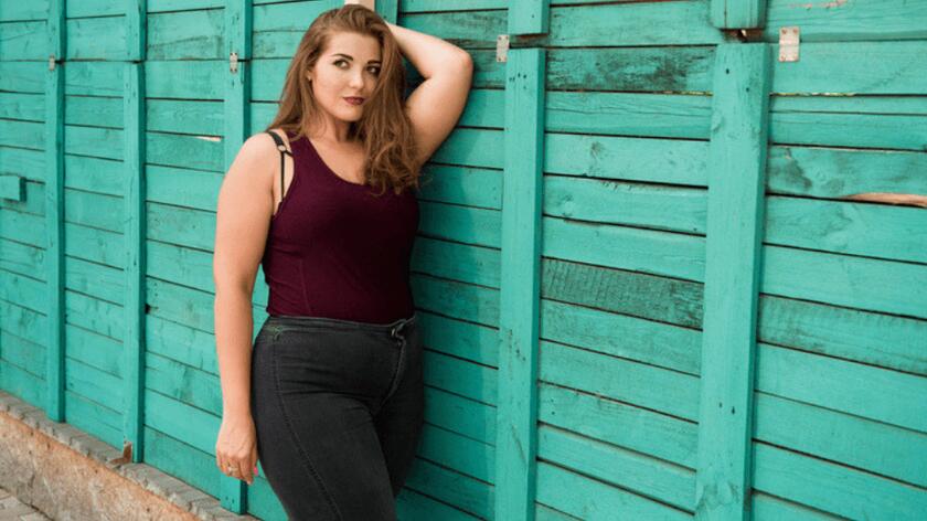 puszysta mloda kobieta plus size w modnych spodniach na tle zielonej drewnianej sciany