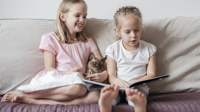 dwie dziewczynki z kotem czytają książkę