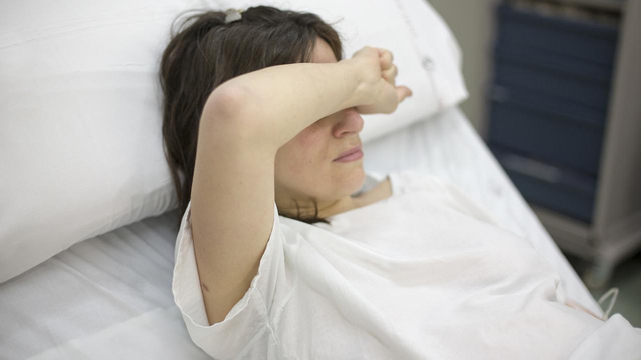 Kobieta w ciąży leży w szpitalu i zasłania reką oczy