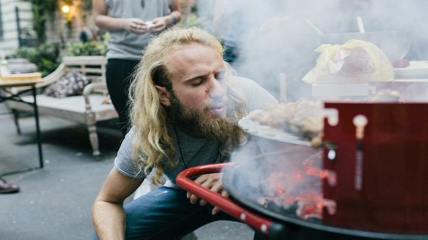 mężczyzna rozpala grilla dmuchając w ogień