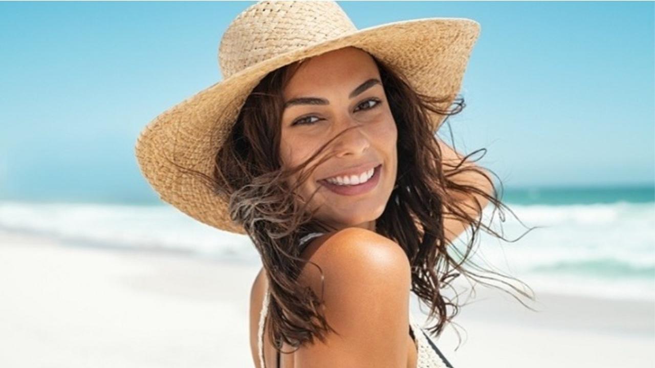 Uśmiechnięta kobieta w kapeluszu na plaży