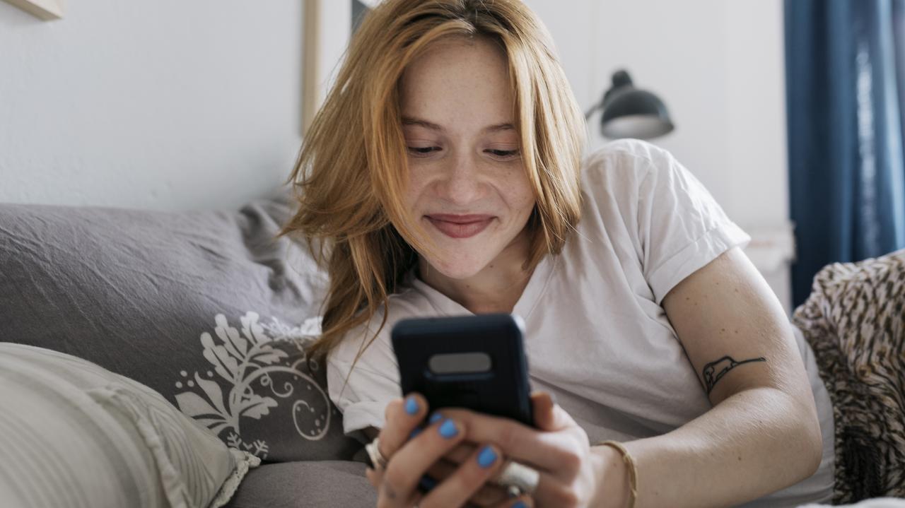 Uśmiechnięta kobieta pochylająca się nad ekranem telefonu
