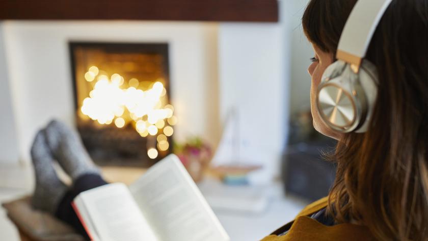 Kobieta słucha muzyki przy kominku i czyta książkę