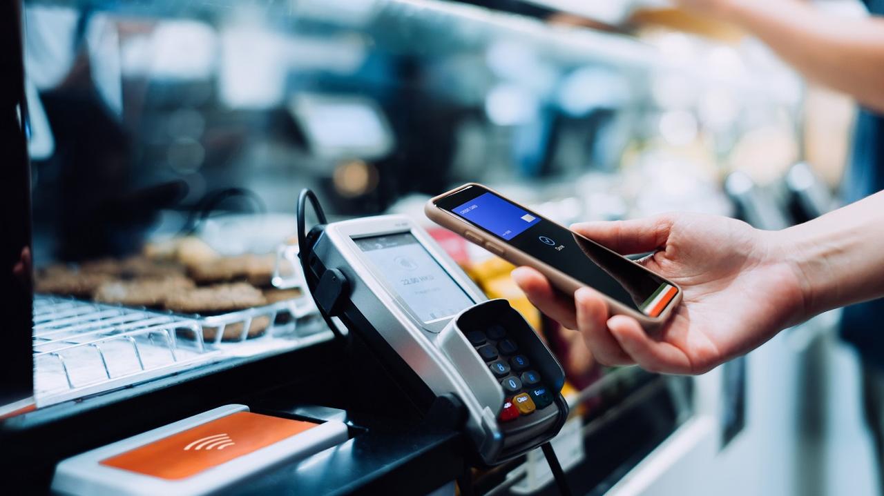 płacenie bezgotówkowe, telefon w dłoni przy terminalu płatniczym w sklepie