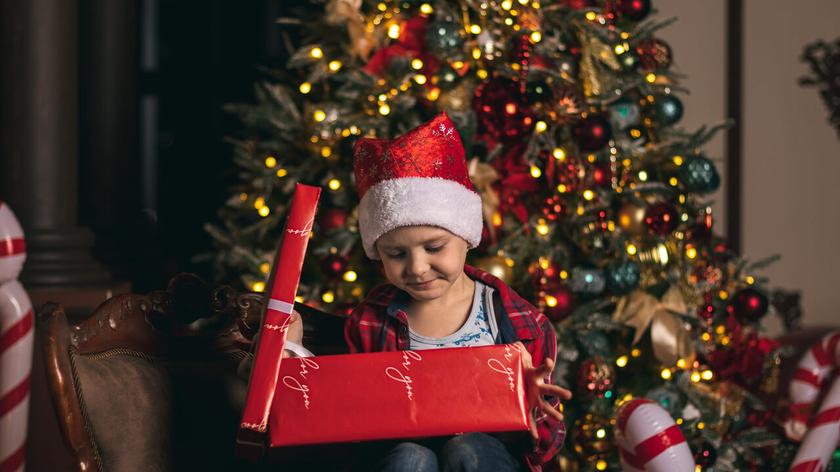 Dziecko otwiera prezent pod choinką