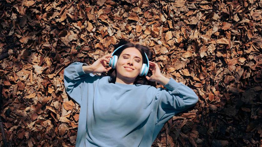 Dziewczyna w słuchawkach leżąca na jesiennych liściach