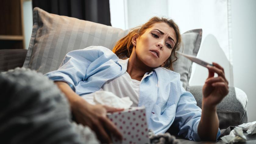 Chora kobieta w łóżku, z termometrem i chusteczkami