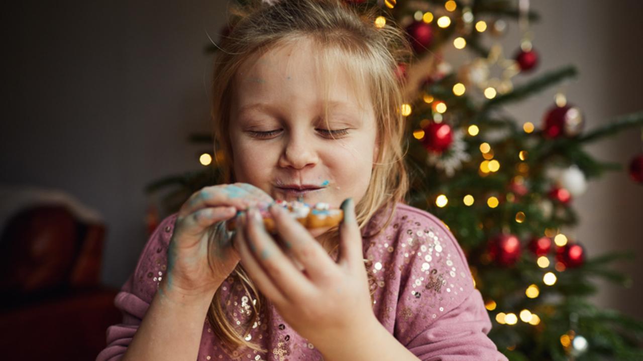 Mała dziewczynka delektująca się lukrowanym piernikiem. Świąteczne potrawy dla dzieci.