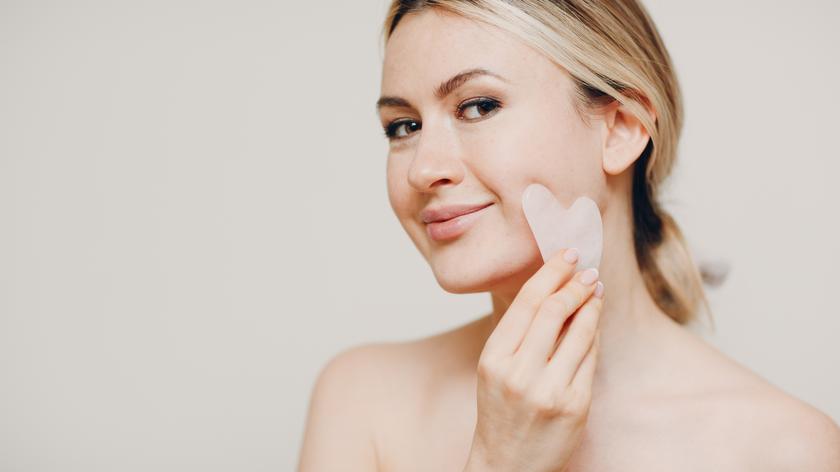 Kobieta wykonująca masaż twarzy masażerem gua sha