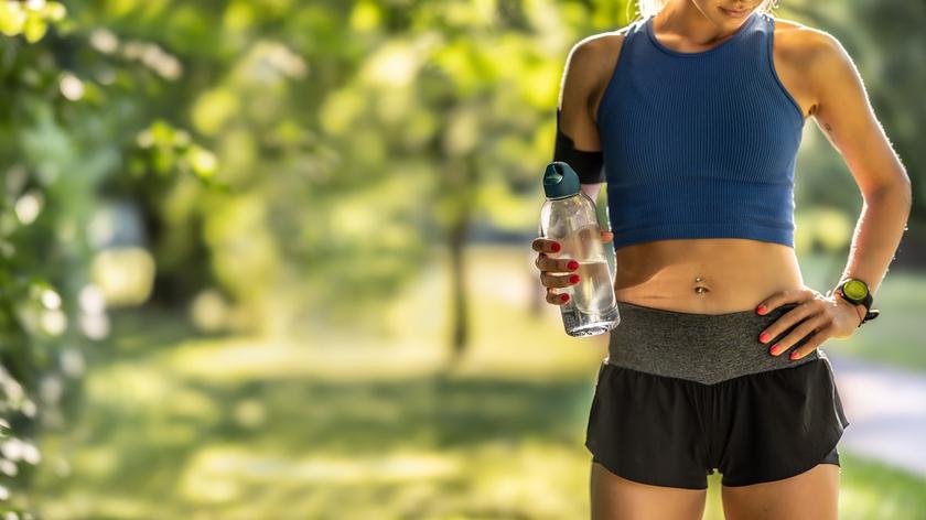 Trening w upał - kobieta z butelką wody, w tle drzewa