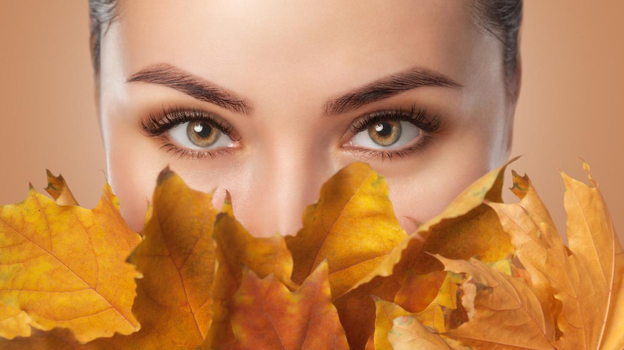 Kobieca twarz przysłonięta jesiennymi liśćmi. Makijaż na jesień. Trendy w makijażu