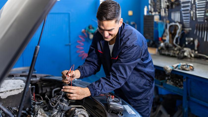Mechanik pochylający się nad otwartą maską samochodu.