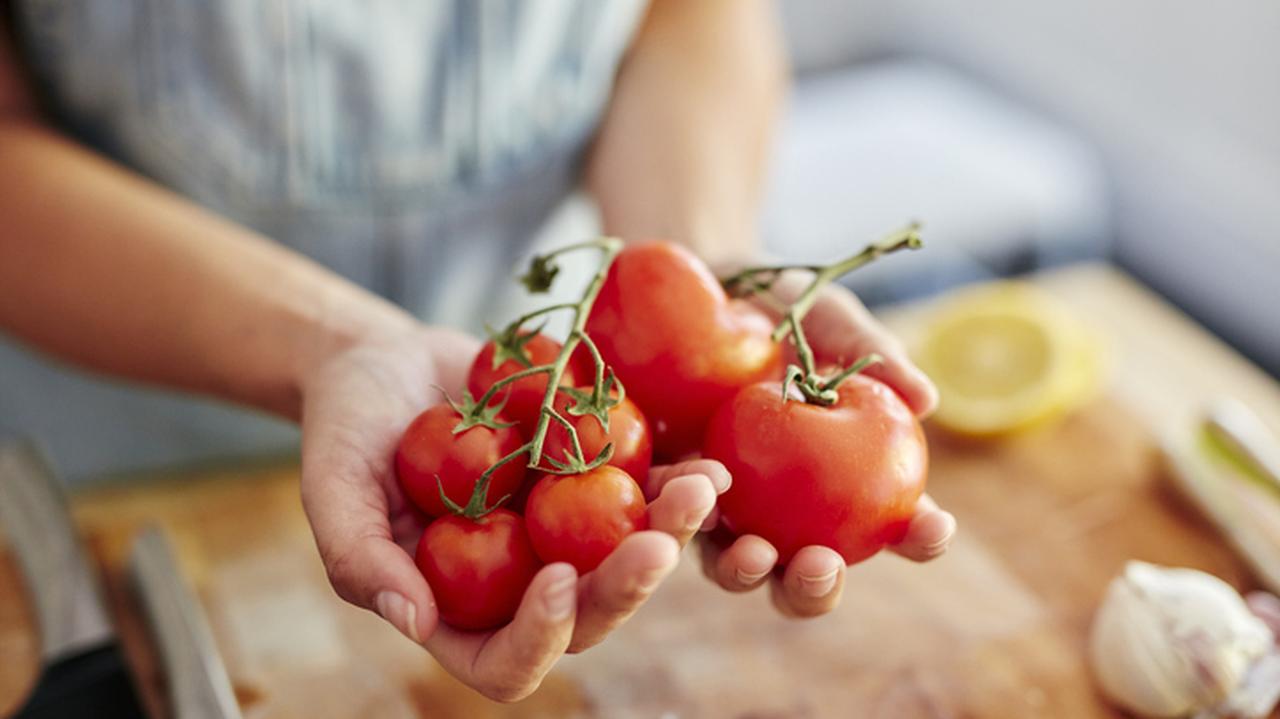 Kobieta trzymająca w dłoniach pomidory w różnych rozmiarach.