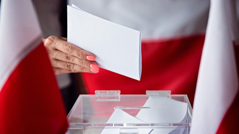 Kobieca dłoń wkładająca kartę do głosowania
