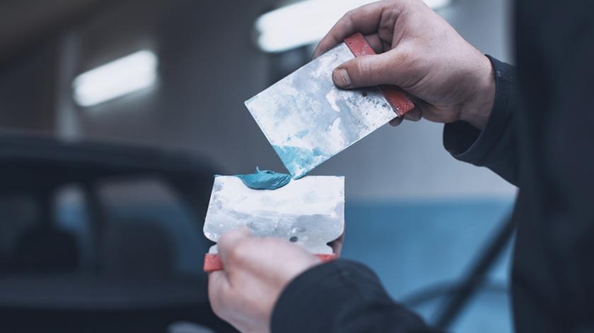 Mężczyzna trzymający w dłoniach szpachlę samochodową. 