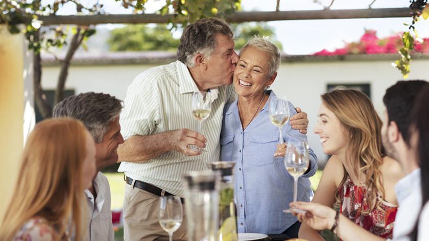 Mężczyzna wznosi toast, składając pocałunek na policzku uśmiechniętej kobiety. Rocznica ślubu. Życzenia.