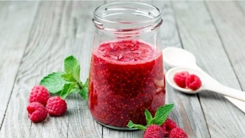 Słoik z syropem i kawałkami malin, obok soczyste owoce z zielonymi listkami