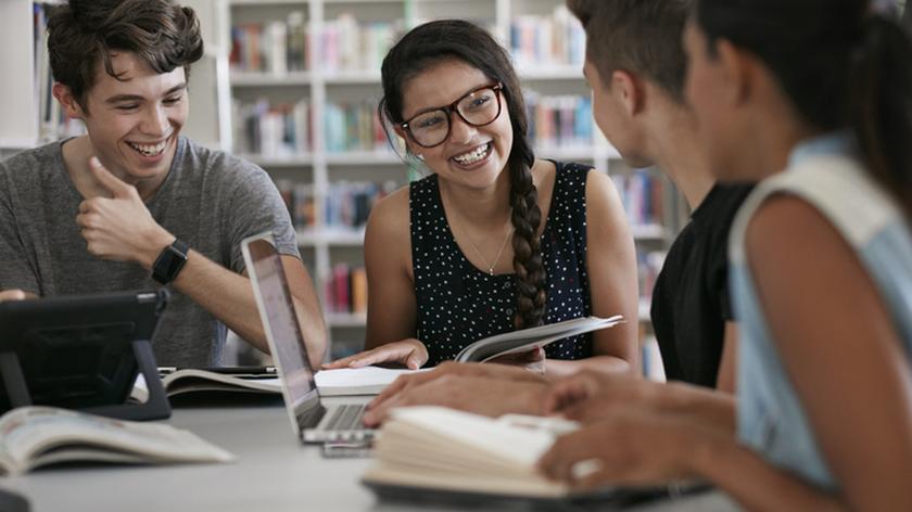 Młodzi ludzie pochyleni nad książkami i ekranami komputerów. Studia technologiczne.