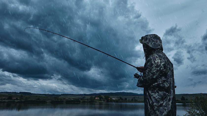 Osoba stojąca z wędką w deszczu nad jeziorem