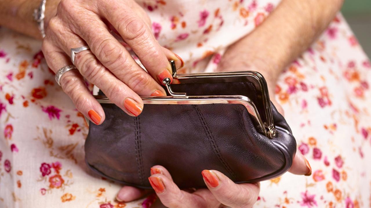 Starsza kobieta w kwiecistej sukni sięgająca do portmonetki. 