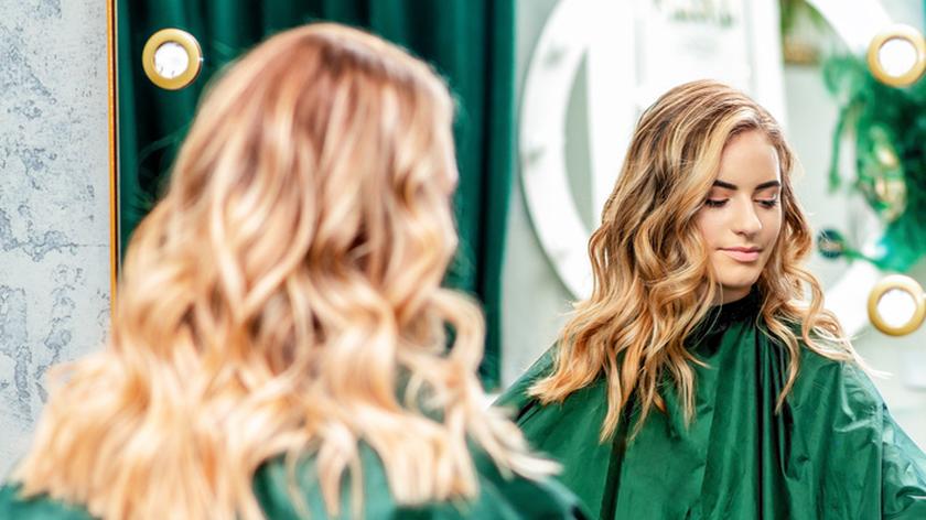 Kobieta siedząca przed lustrem w salonie fryzjerskim. Ribbon blond. Modne kolory włosów.