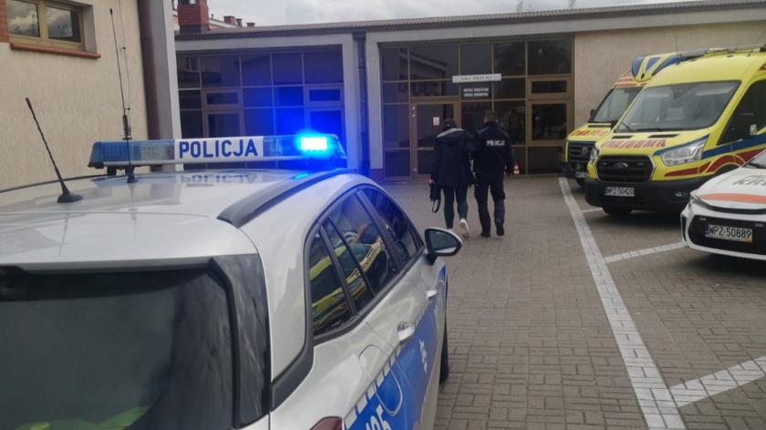 Radiowóz przed szpitalem. Policjant prowadzi ciężarna kobietę na porodówkę. 