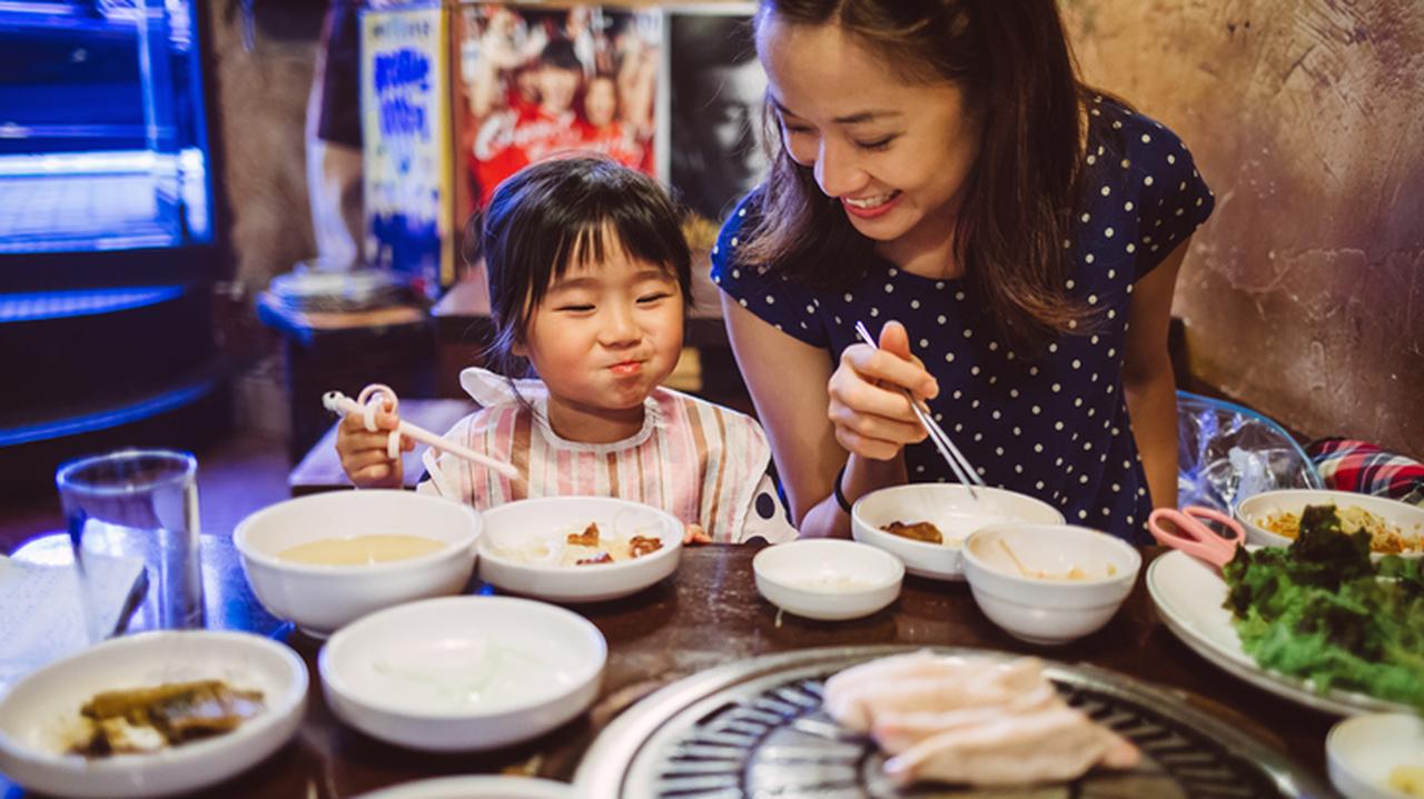 Uśmiechnięta kobieta z dzieckiem nad suto zastawionym stołem. Kuchnia koreańska. Przepisy kulinarne.