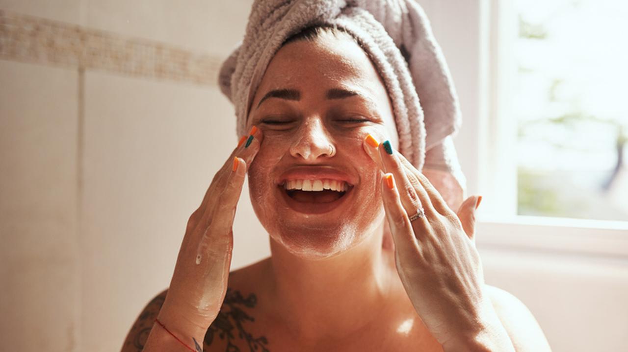 Uśmiechnięta kobieta myjąca twarz. Detoks skóry. Pielęgnacja skóry. Domowa pielęgnacja.