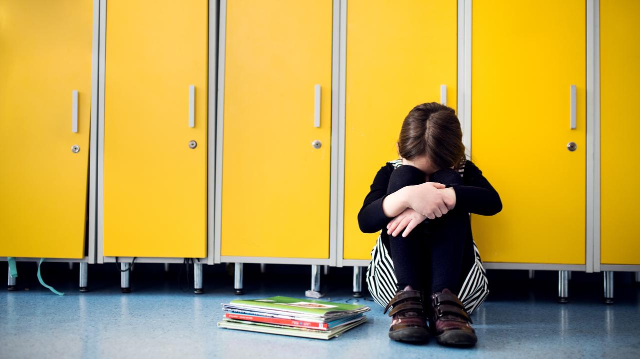 Dziewczynka, która siedzi na podłodze w szkole i płacze 